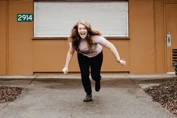 Woman smiling and running playfully toward the camera on a paved walkway.