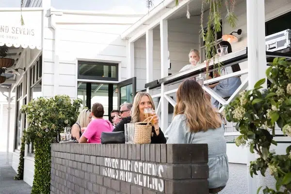 Friends socializing and enjoying drinks on the sunny outdoor patio of the Sixes and Sevens gastro pub.