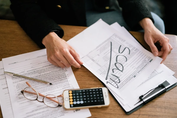 Hands reviewing property paperwork at a desk with the word Scam written across one of the documents, beside glasses, a pen and a phone